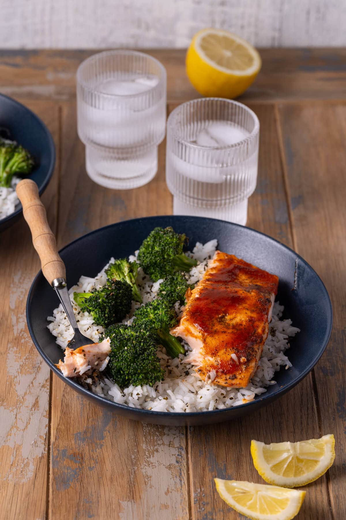 Sriracha honey salmon with a bite on a fork served with broccoli and rice. 