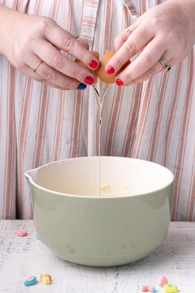 Cracking an egg into a mixing bowl with creamed butter and sugar and vanilla extract.