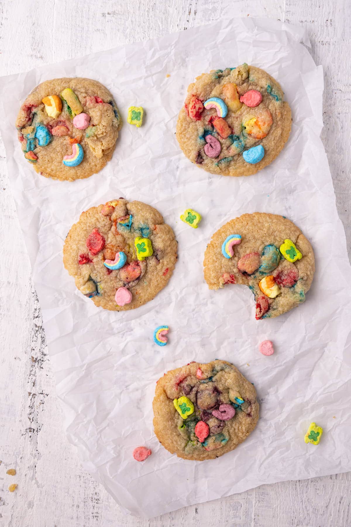Six just-baked Lucky Charms cookies, one with a bite taken out. 