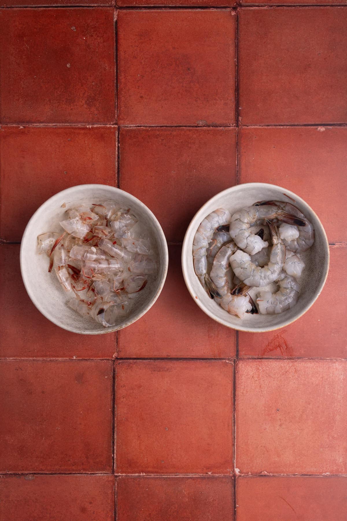 Raw shrimp peeled and shells in a separate bowl. 