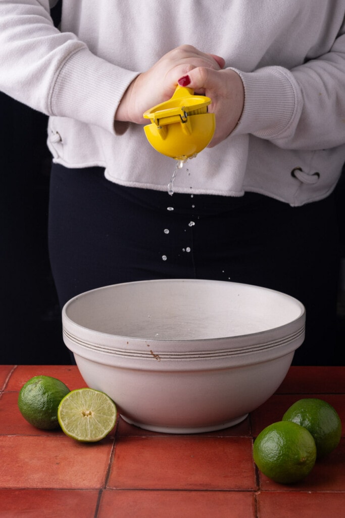 Squeezing lime juice into a large bowl with tequila and taco seasoning.