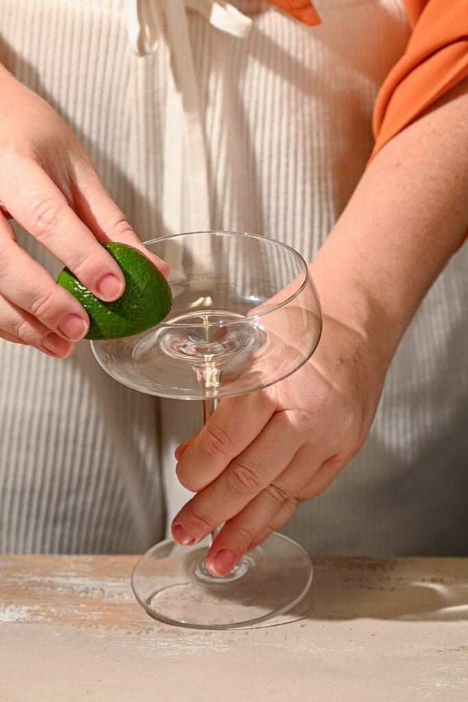 Using a halved lime to wet the rim of a coupe glass. 
