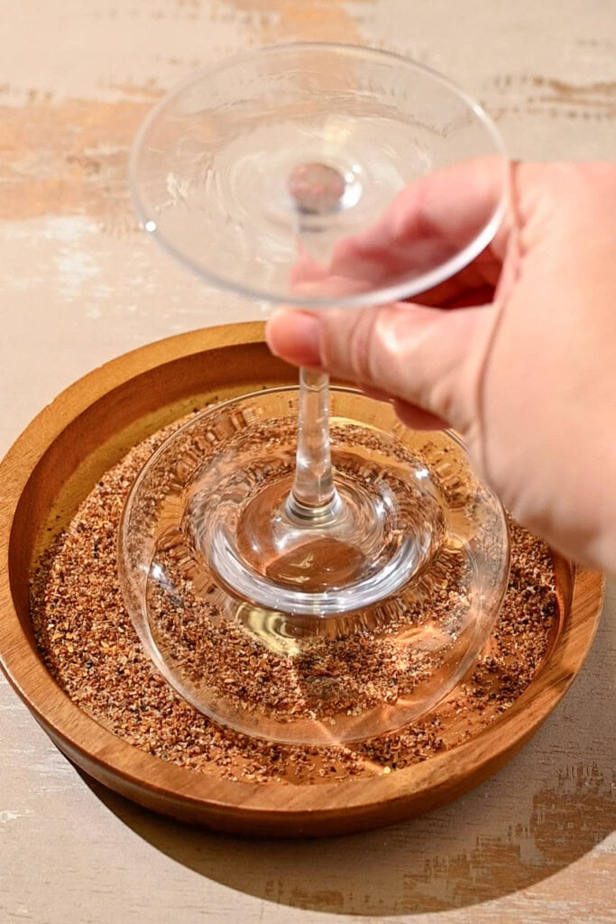 Dredging the wet rim of a coupe glass through tajin. 