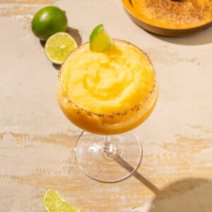 Coupe glass filled with thick frozen peach margarita with tajin rim.