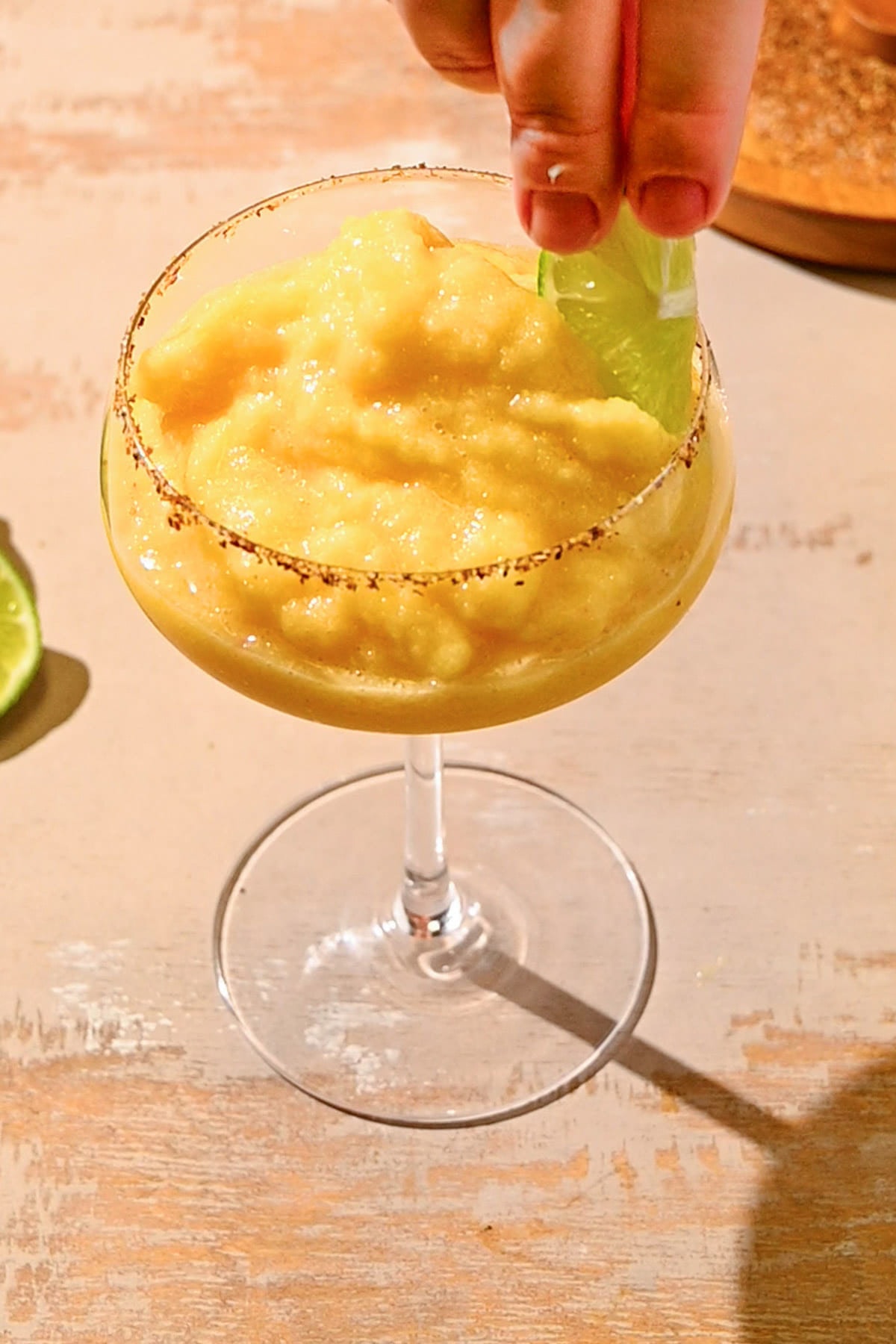 Garnishing a frozen margarita with peaches with a lime wedge. 