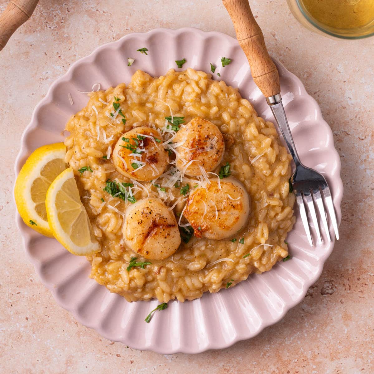 Scallop risotto served with lemon wedges on a pink plate.