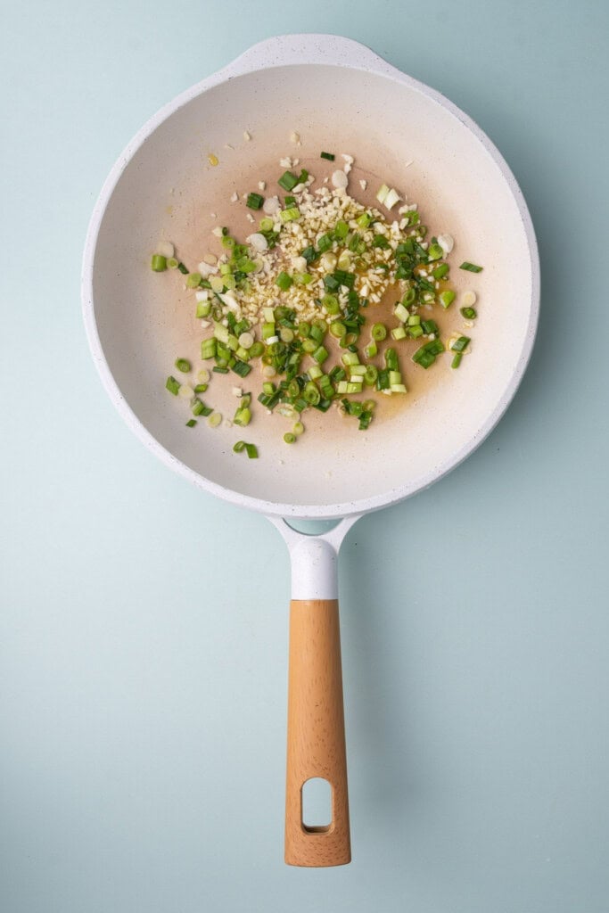 Cooking minced garlic and diced scallions in hot olive oil.