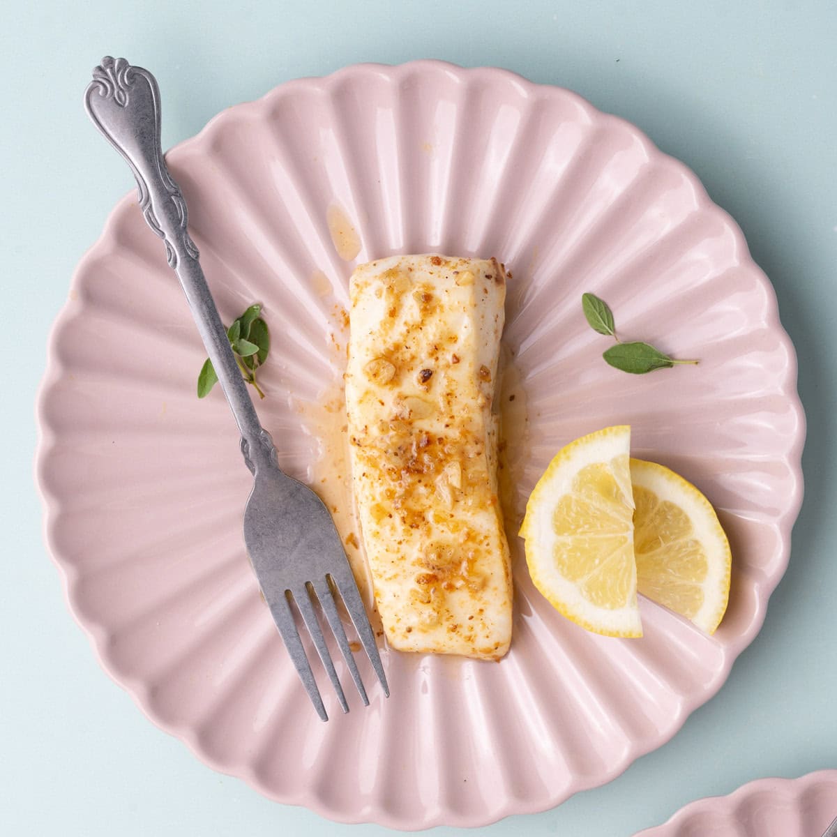 Ribbed pink plate with butter-basted halibut and two lemon wedges.