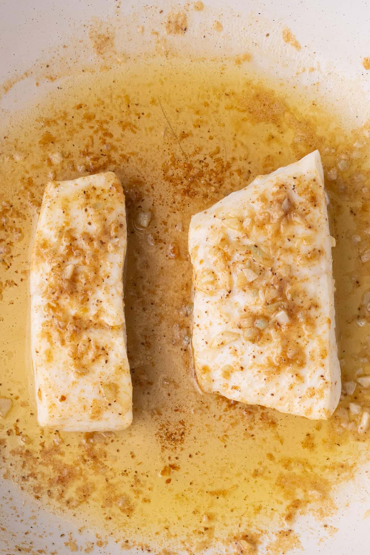 Close up of garlicky halibut in a pan with hot butter and lemon.
