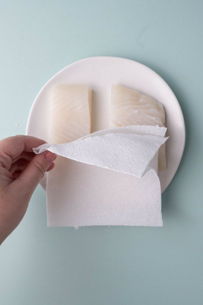 Patting halibut dry with a paper towel to prep for pan frying.