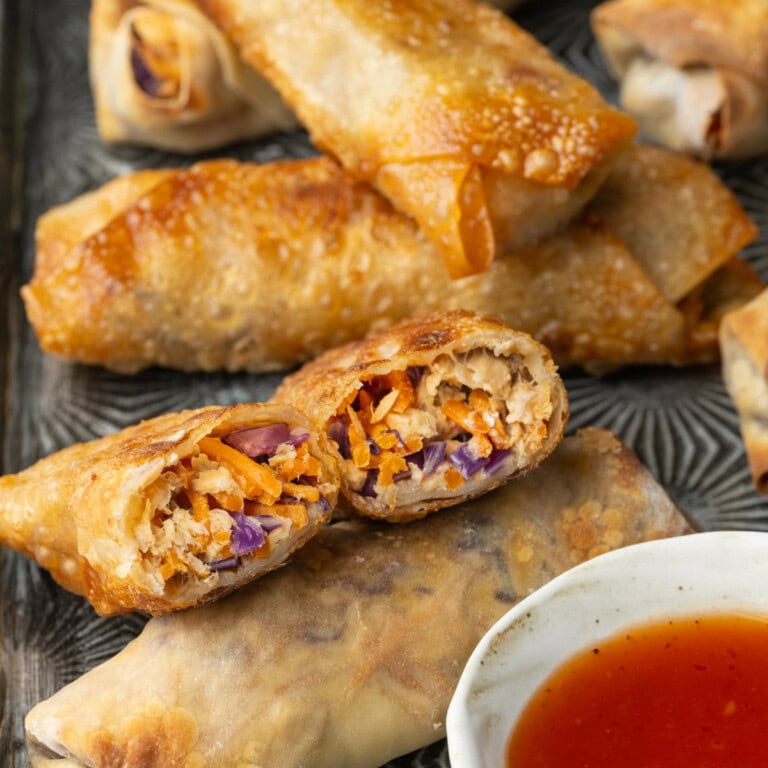 Egg rolls with salmon on a metal serving tray with a bowl of sweet Thai chili sauce.