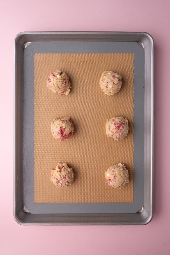 Cookie dough shaped into spheres and lined up on a baking sheet. 