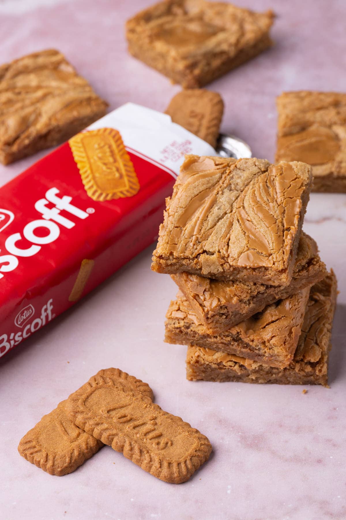 Cookie butter swirled blondies stacked atop one another with a package of biscoff cookies behind it. 