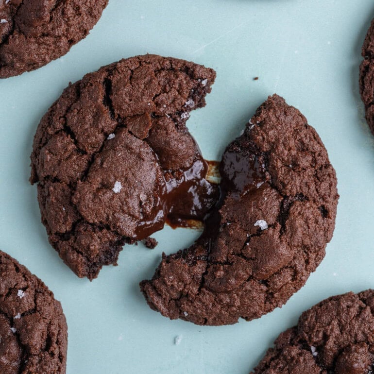 Molten chocolate fudge cookie broken open to reveal gooey center on a blue background.