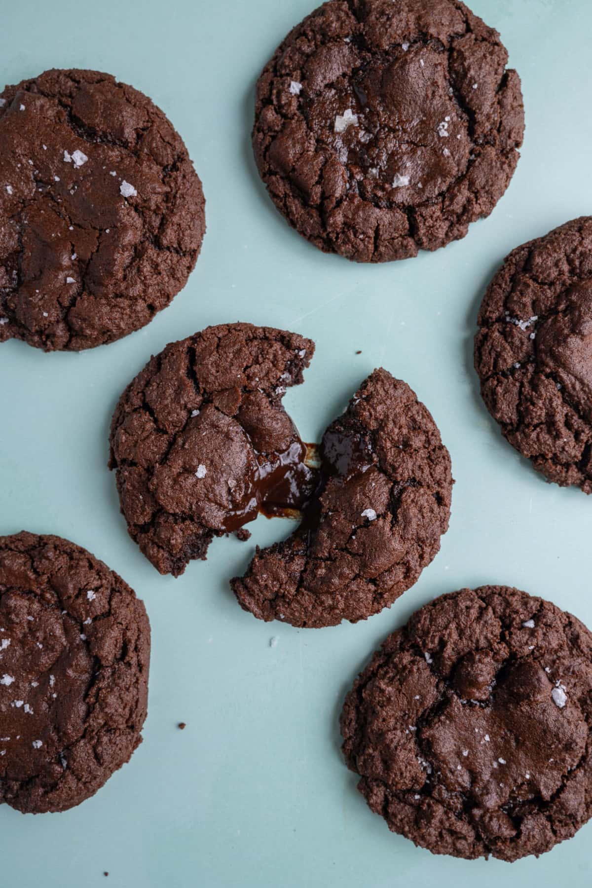 Overhead image of chocolate fudge cookies with middle one pulled apart to reveal molten chocolate center.