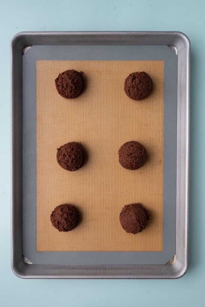 Chocolate cookie dough shaped and lined up on a large cookie sheet. 
