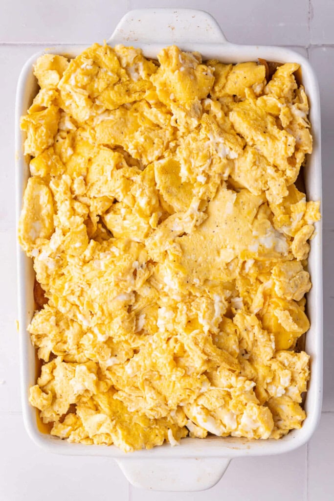 Scrambled eggs in a casserole dish with onion and cheese on Hawaiian rolls.