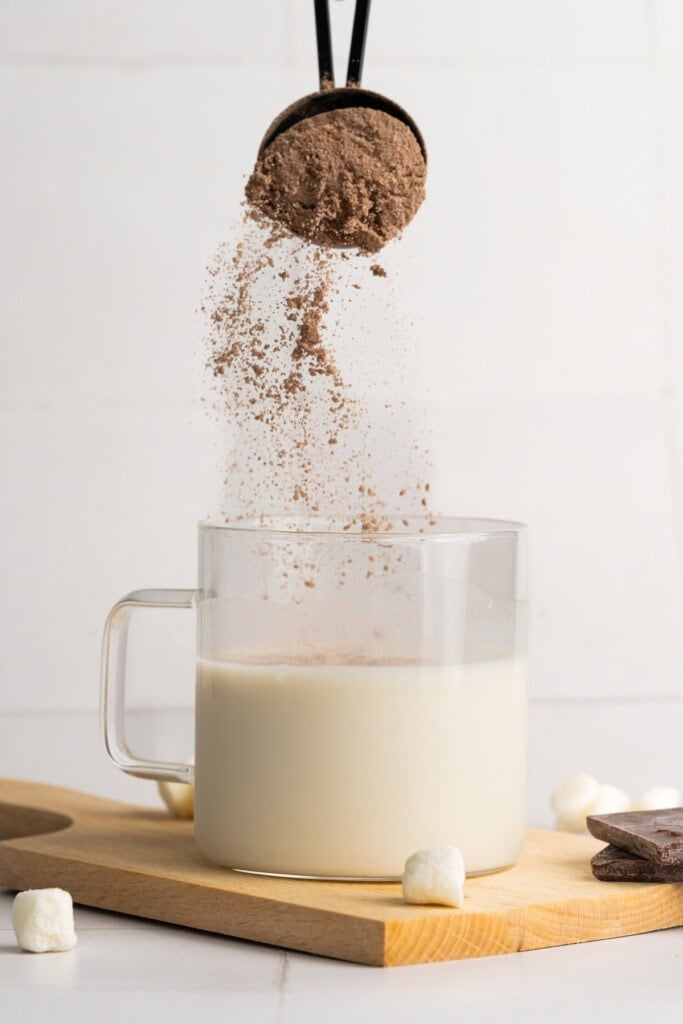 Adding hot chocolate mix to warm milk in a mug.