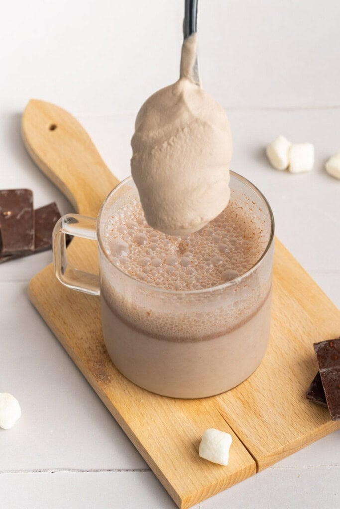 Adding whipped hot chocolate on top of regular hot cocoa with a spoon.