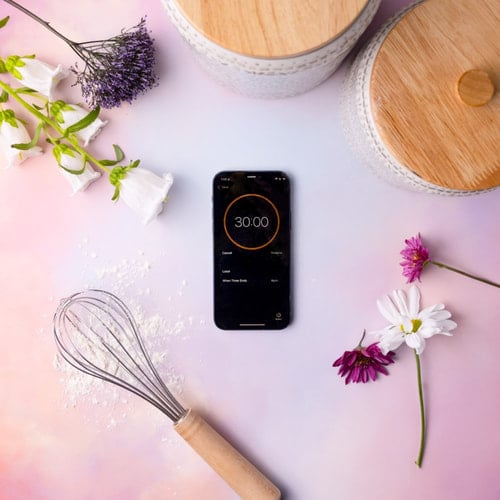 Overhead view of a cell phone showing a 30 minute timer surrounding with kitchen objects.