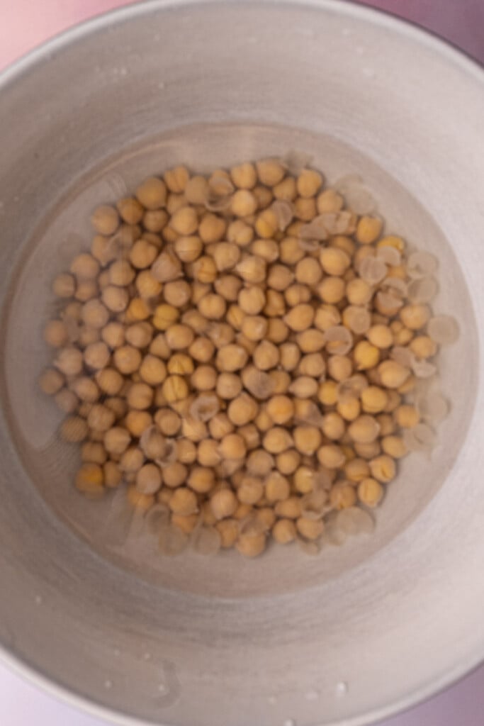 Chickpeas submerged in water with the separated skins floating towards the top of the surface. 