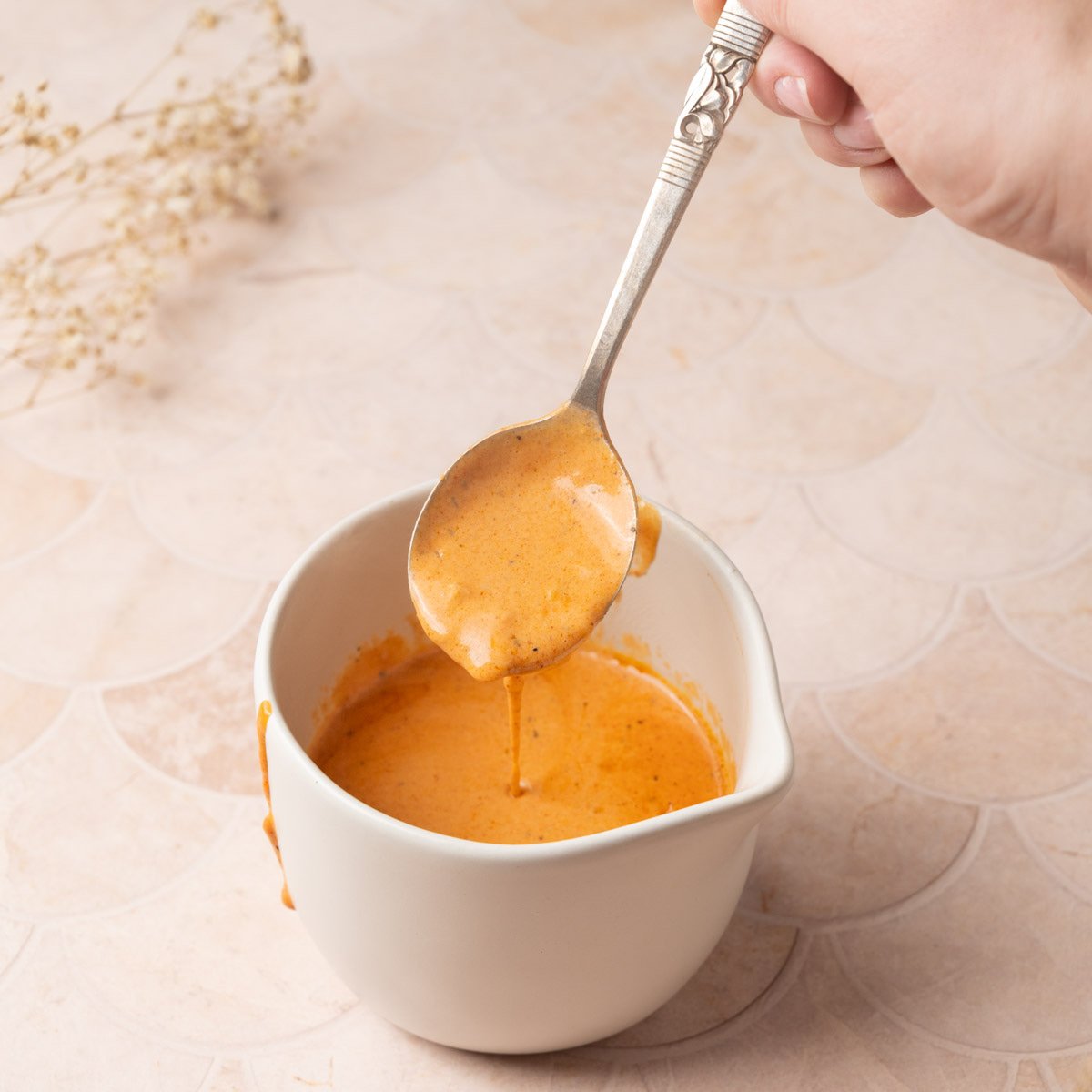 Cajun Cream Sauce running off a spoon into a jug to show the smooth texture.