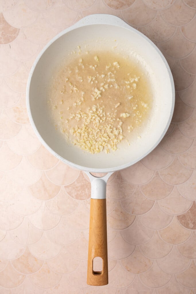 Minced garlic cooking in butter in a white pan.