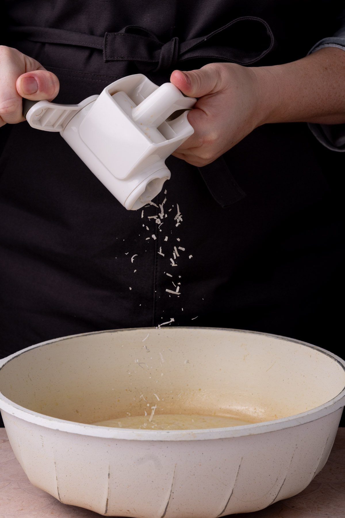 Adding Parmesan to a pan with vegetable broth and cream.