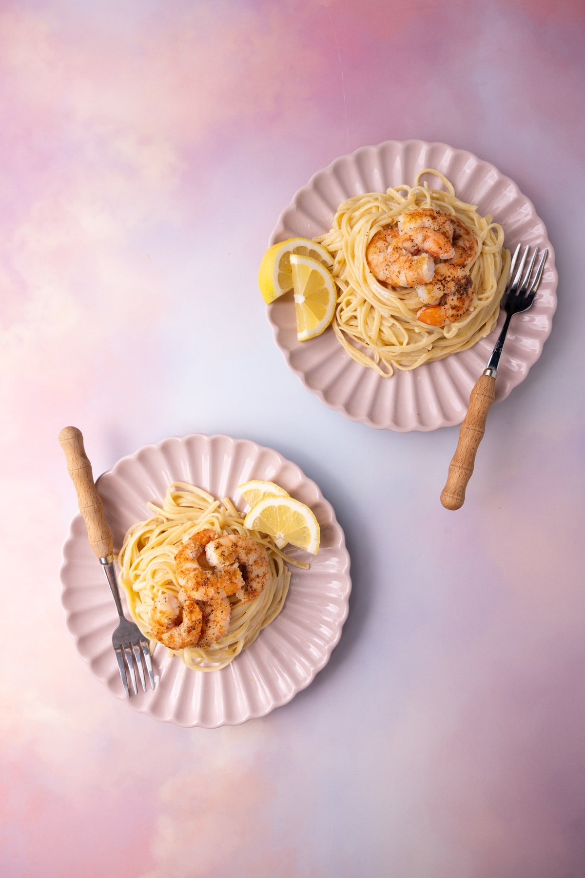 Two plates of creamy garlic shrimp pasta on a colorful background served with lemon wedges. 