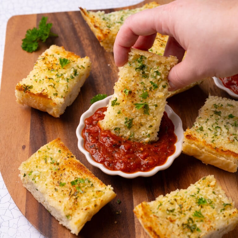 Piece of garlic bread dunking into marinara sauce for dipping.