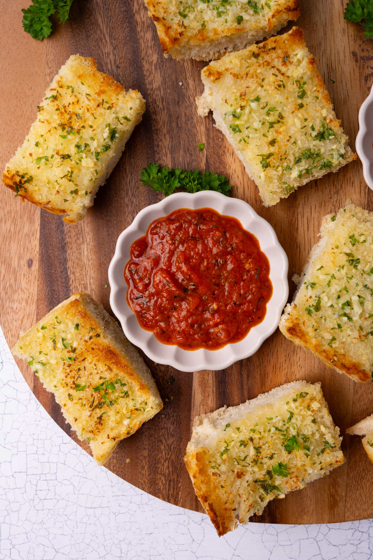 Marinara dipping sauce on a wooden board surrounded by garlic bread. 