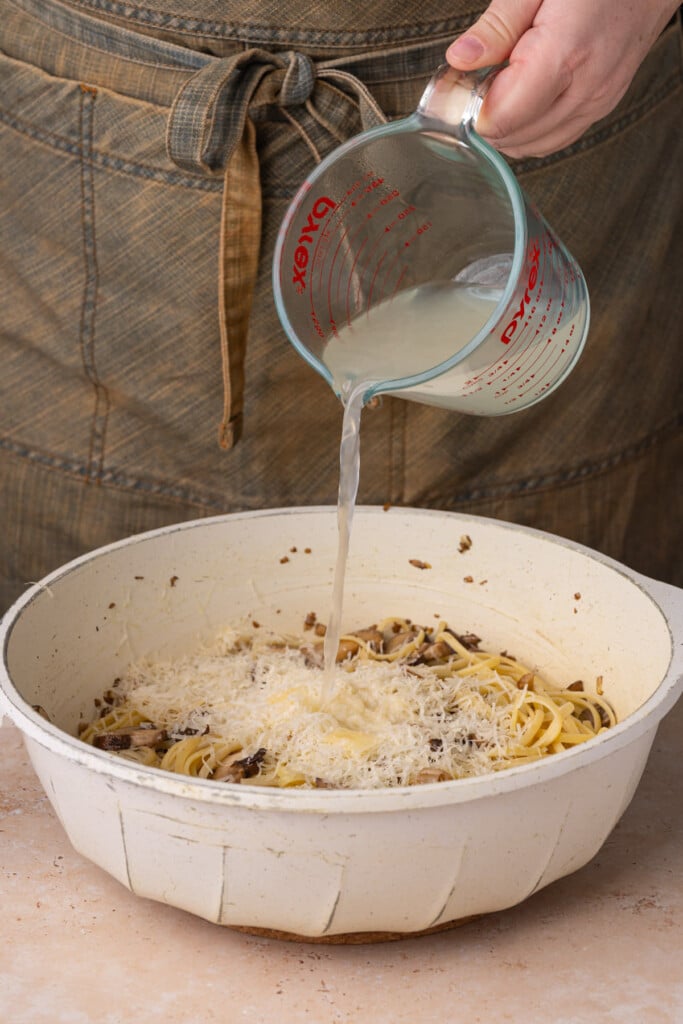 Adding pasta water to mushroom and Parmesan pasta to thin out. 