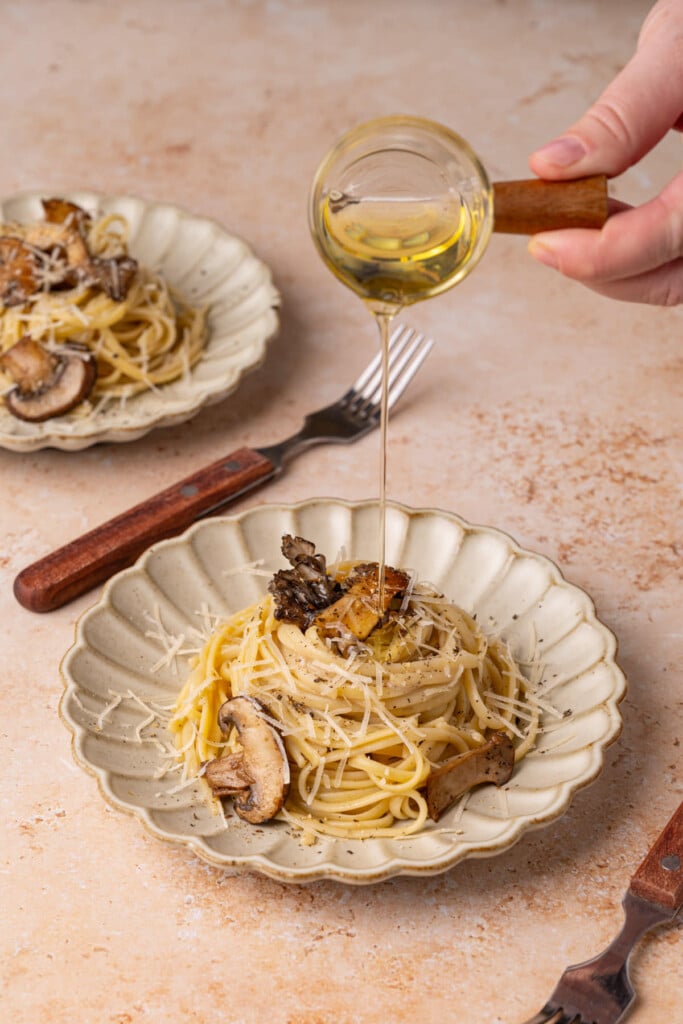 Pouring truffle oil over individual portion of pasta.