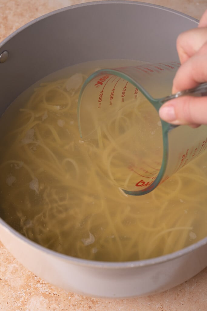 Taking pasta water out to save before draining boiled pasta. 