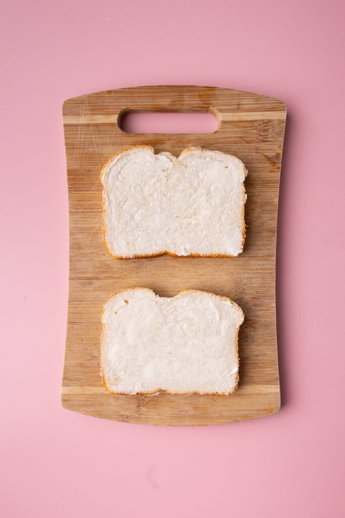 Two slices of sandwich bread with an even layer of butter on one side.