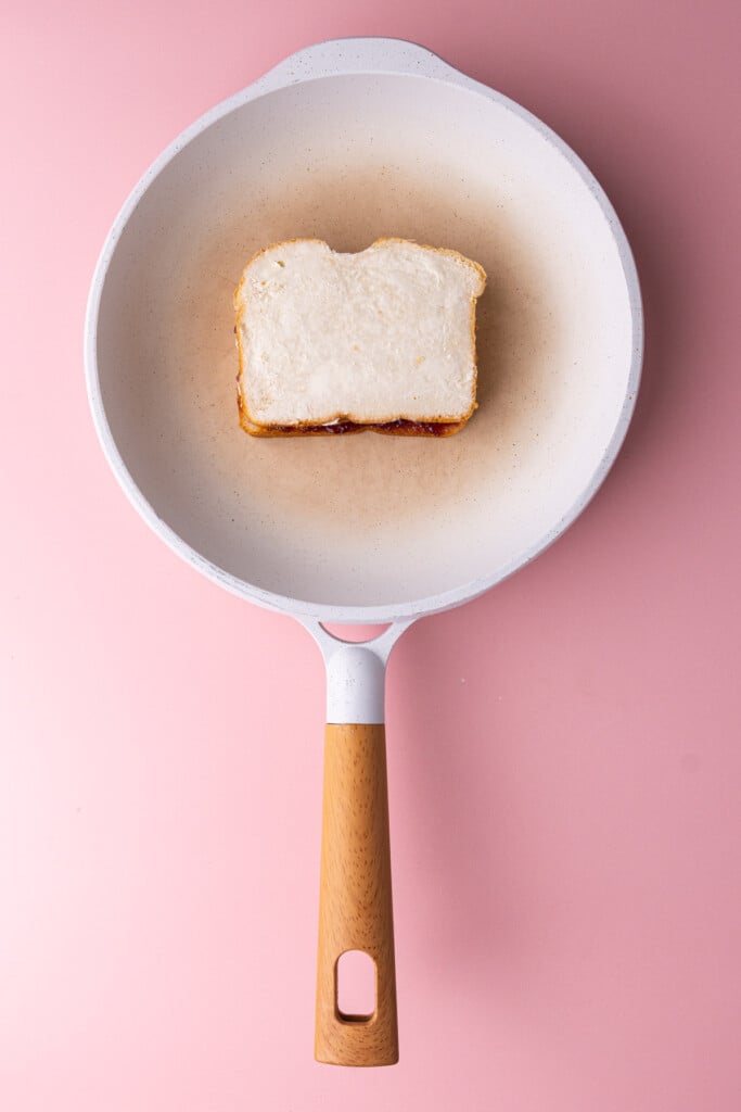 Peanut butter and jelly sandwich frying in a pan.
