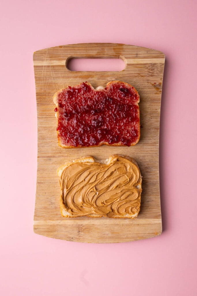 Two slices of sandwich bread, one with grape jelly and the other with creamy peanut butter.
