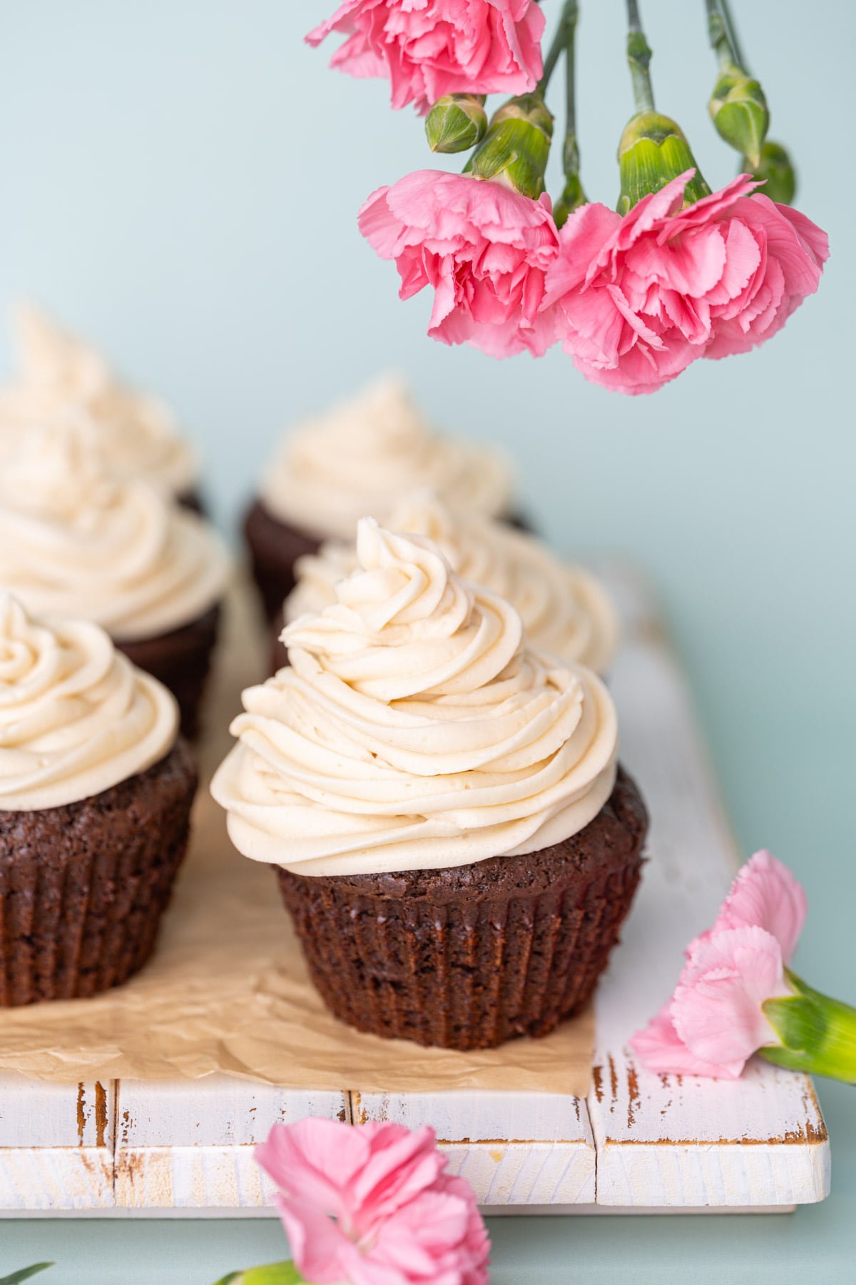 Close up of cupcake topped with Irish Cream frosting with pink flowers around it. 