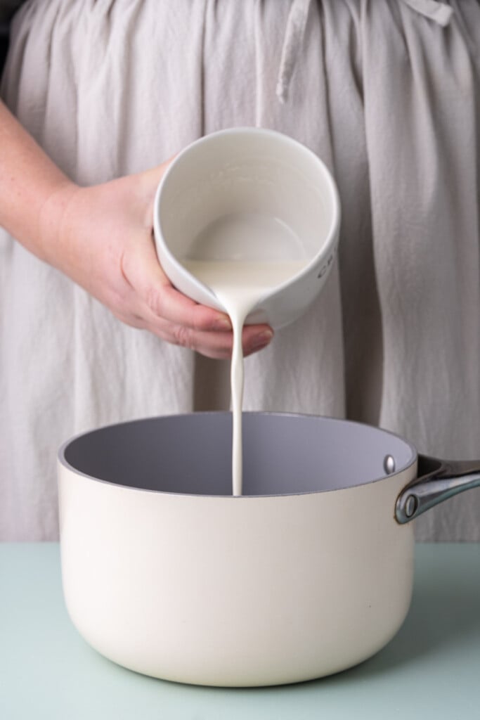 Adding heavy whipping cream to a saucepan to heat up on the stove. 