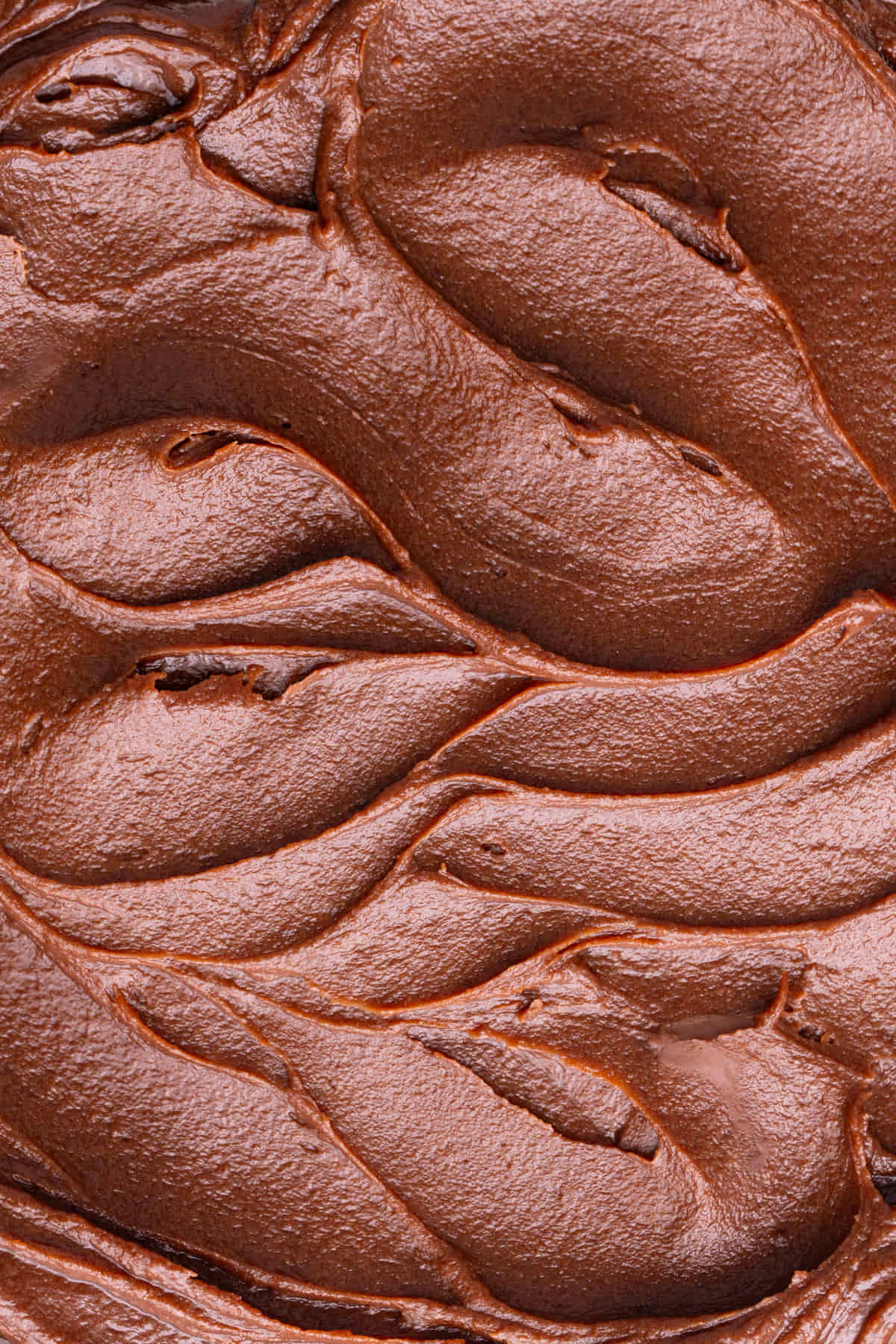 Close up of thick and spreadable milk chocolate ganache with swirls made with a spatula to show the texture. 