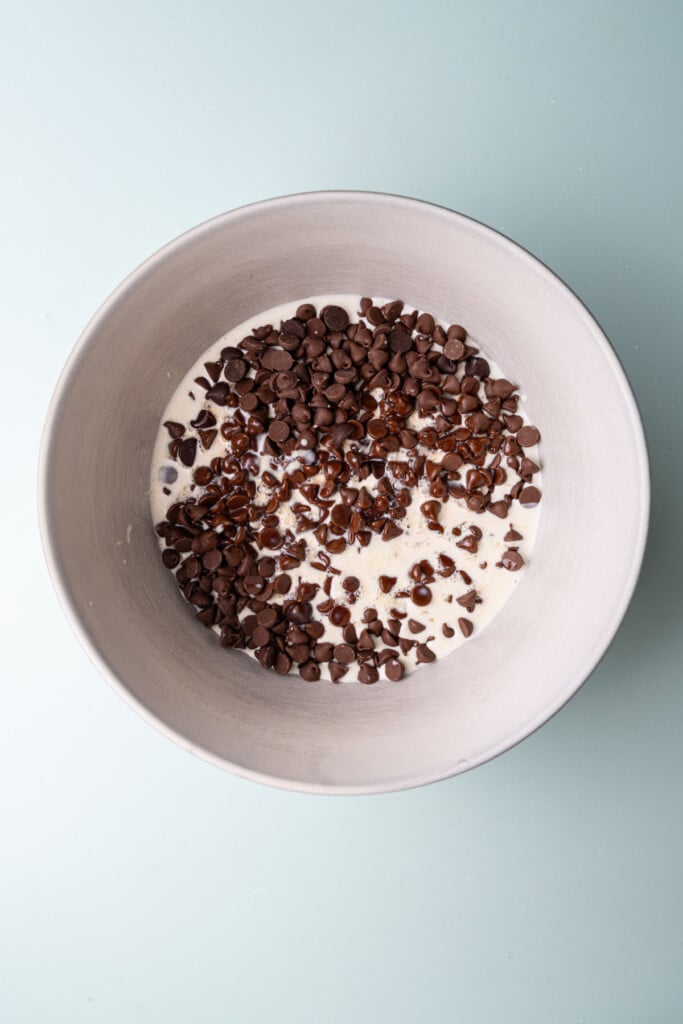 Allowing warm cream to melt chocolate chips in a bowl by letting them sit together. 