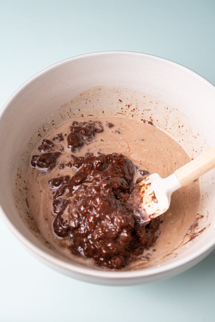 Using a spatula to stir together melting milk chocolate chips and warm heavy cream.