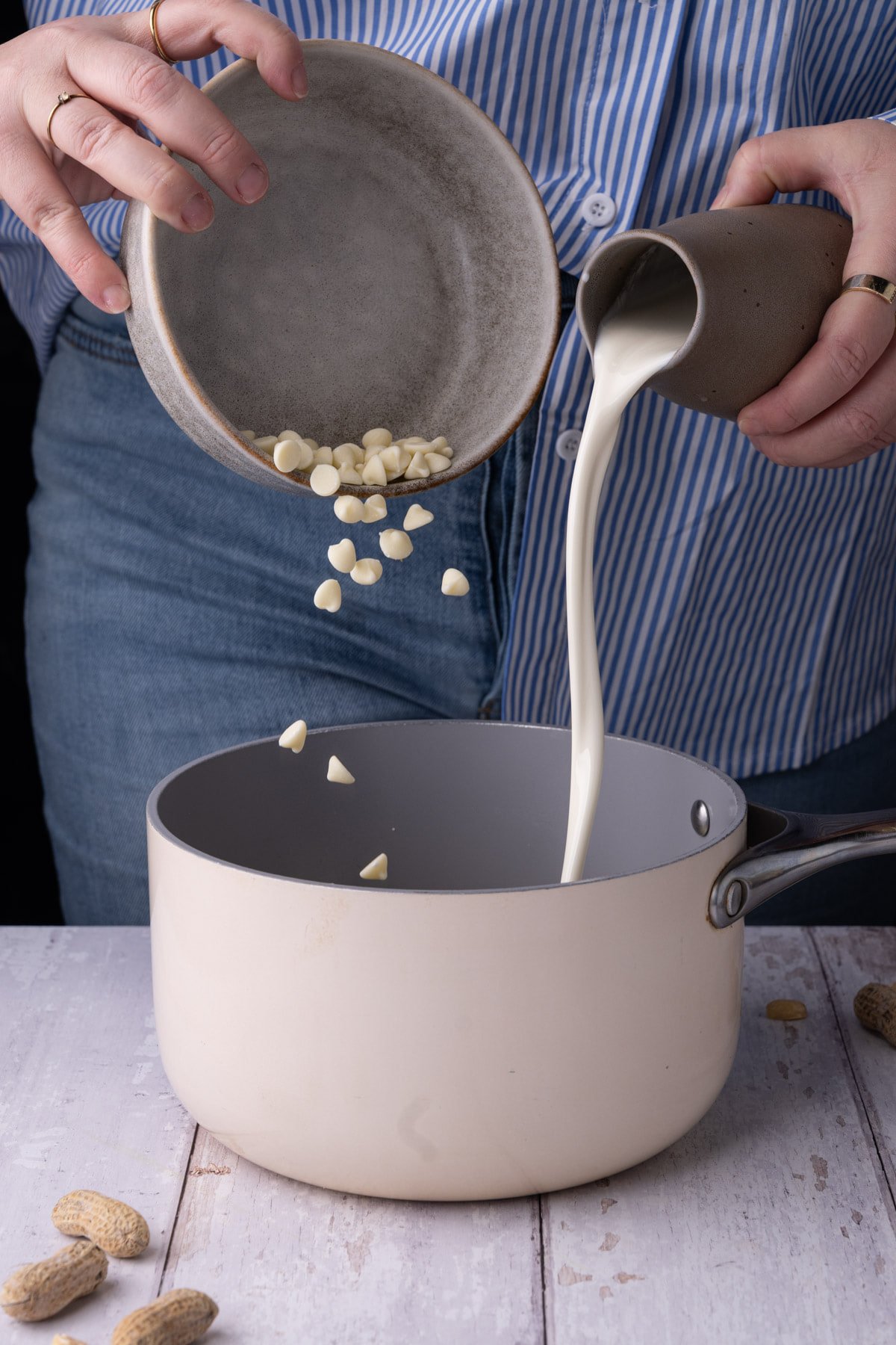 Pouring cream and white chocolate chips into a pot to melt down with peanut butter. 