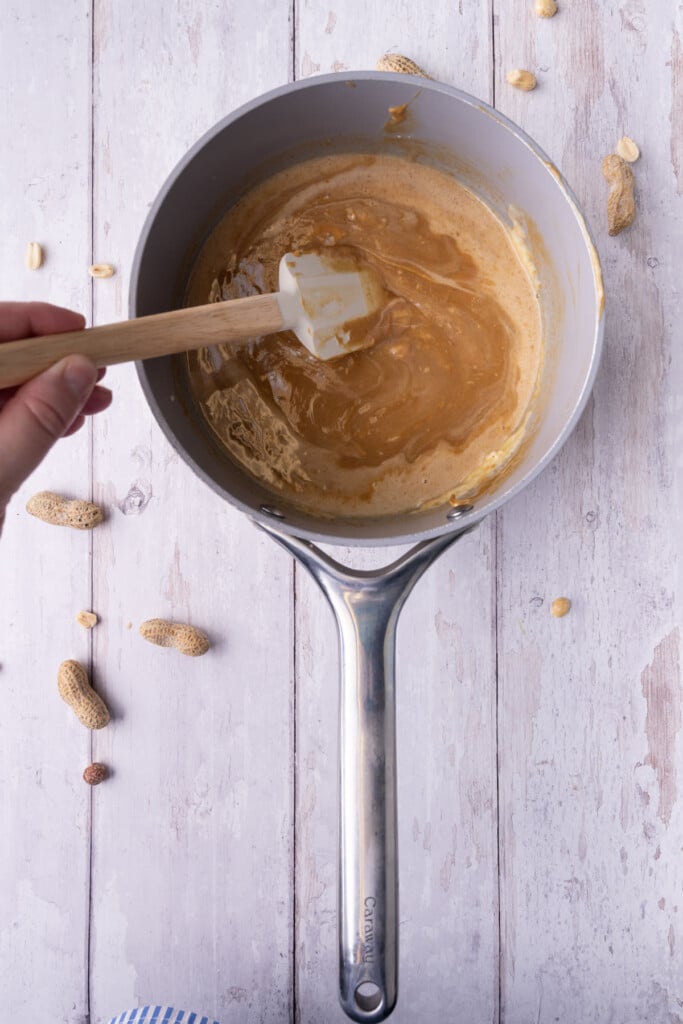 Slowly stirring together cream, white chocolate chips, and peanut butter in a pot over medium heat. 