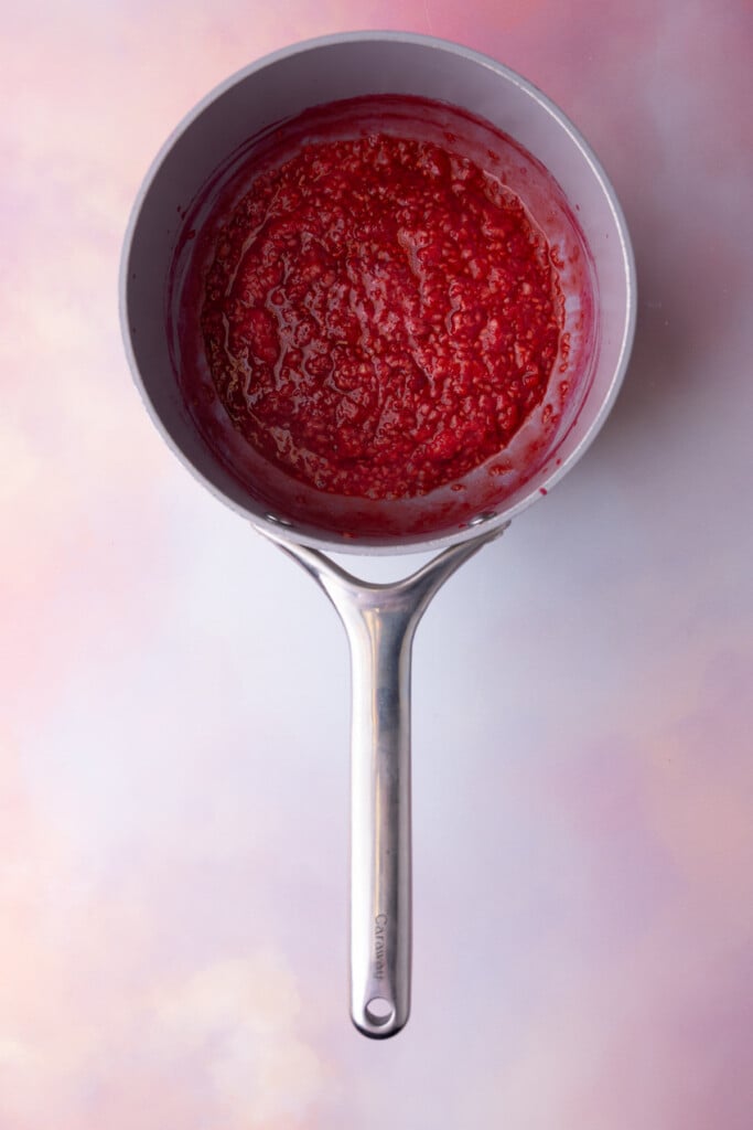 Boiled raspberries broken down into a jam in a pot.