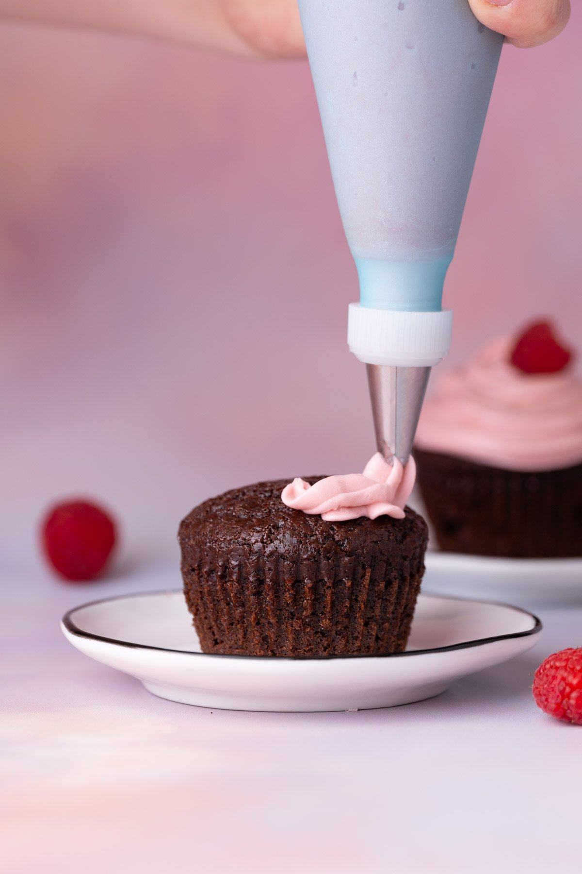 Using a piping bag to pipe raspberry frosting onto chocolate cupcakes. 
