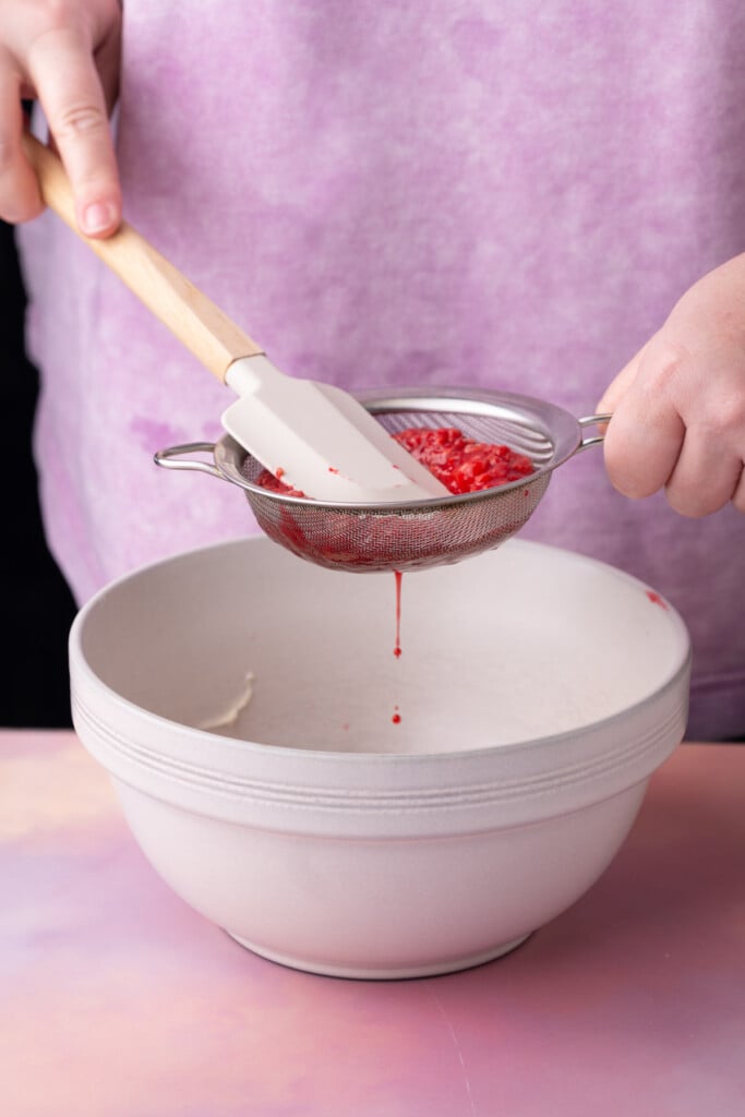 Straining boiled raspberries through a sieve to extract the juice. 