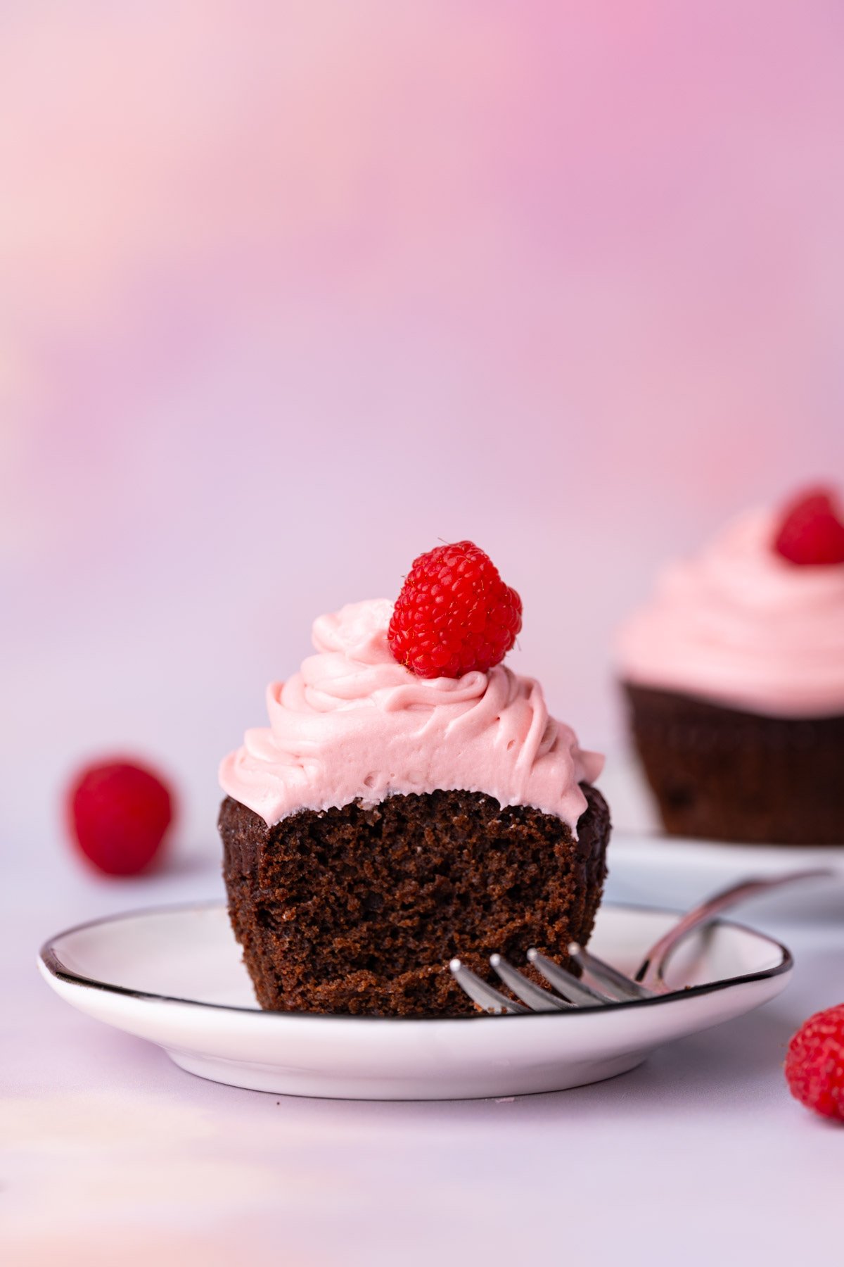 Chocolate cupcake with raspberry buttercream topped with a fresh raspberry with forkful taken out. 