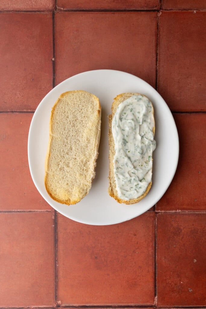 Spreading tartar sauce evenly over bottom bun or a hoagie roll. 
