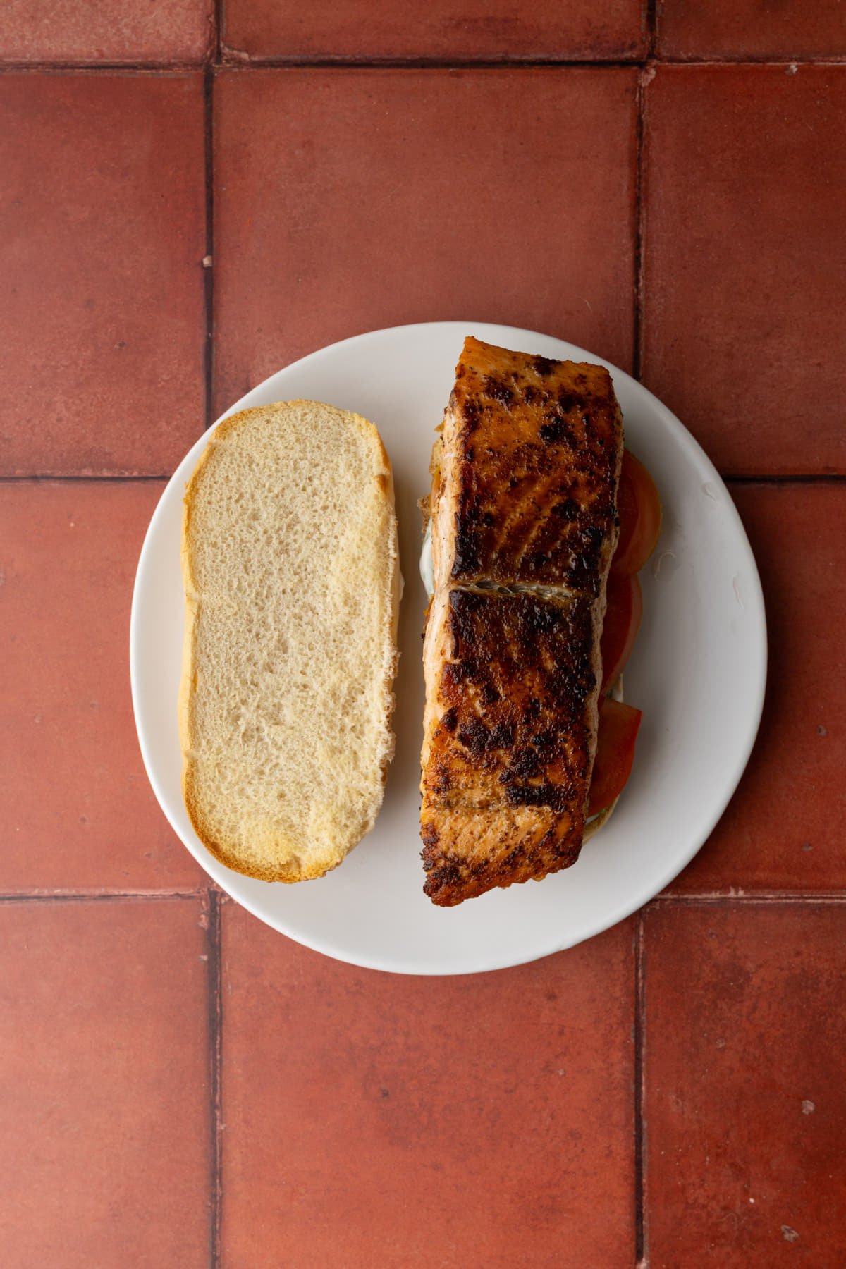 Seared salmon stacked atop sandwich fillings and bread smeared with tartar sauce. 